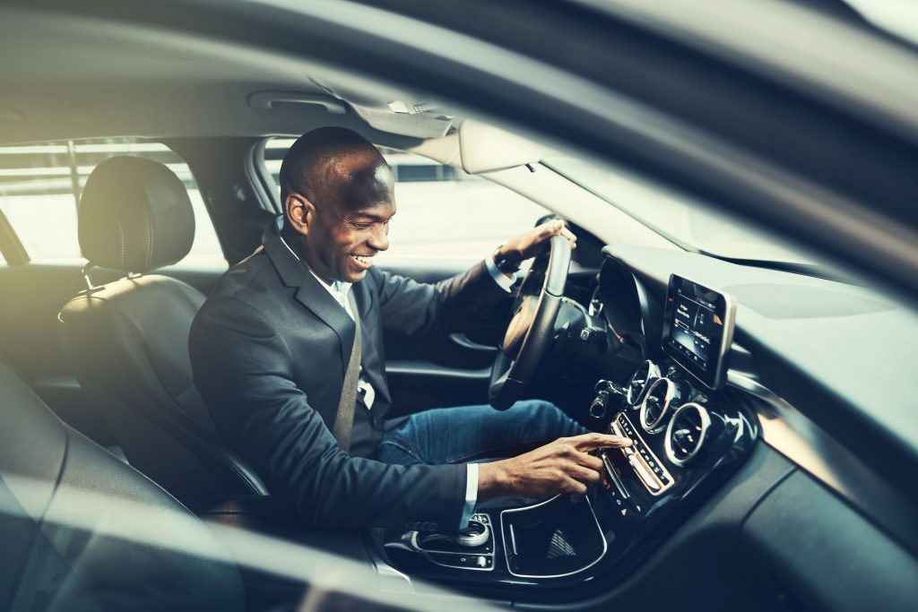 Smiling African businessman changing stations on his car radio while driving through the city during his morning commute to work